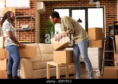 Coppia afroamericana che disimballano le scatole in movimento insieme in una casa a muro di mattoni. Marito e moglie parlano mentre organizzano gli effetti personali pieni durante il giorno del trasloco in un accogliente appartamento moderno. Foto Stock