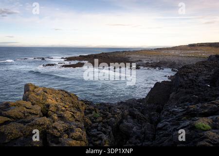 Costa irlandese rocciosa con scogliere scure e onde oceaniche sotto un cielo soffice e nuvoloso Foto Stock