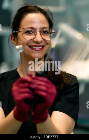 Tecnico di laboratorio sorridente che indossa occhiali con attrezzi chirurgici in un laboratorio moderno durante la sessione di lavoro Foto Stock