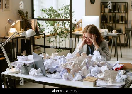Giovane donna adulta che si sente stressata mentre lavora alla scrivania Foto Stock