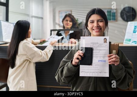 Ritratto di una donna ispanica sorridente in possesso di una domanda di visto approvata e di un passaporto al centro visti Foto Stock