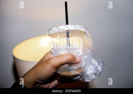 primo piano della mano che regge il latte del caffè ghiacciato sulla tazza di plastica Foto Stock