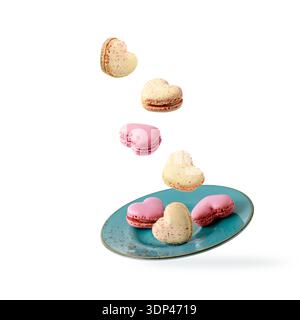 Biscotti francesi a forma di cuore, macaron, macaron che volano su un piatto gren blu vintage isolato su sfondo bianco. Scheda pasticceria Foto Stock