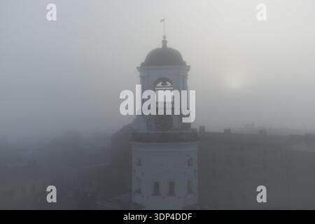 Vyborg, Russia - 19 settembre 2022: Un'antica torre dell'orologio con una campana nel centro storico della città di Vyborg durante la fitta nebbia. Un oggetto del cul Foto Stock