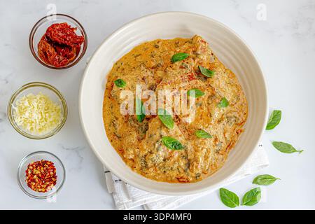 Pollo cremoso in stile toscano con basilico fresco su sfondo chiaro Foto Stock