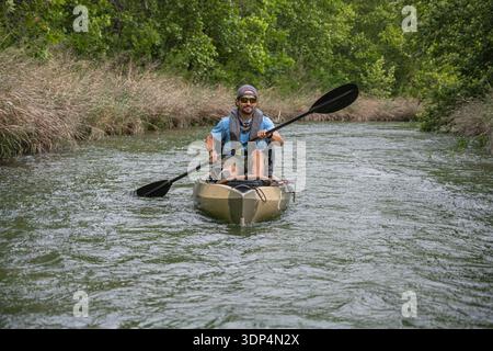 Uomo sorridente pagaiando in kayak lungo un fiume panoramico in estate Foto Stock