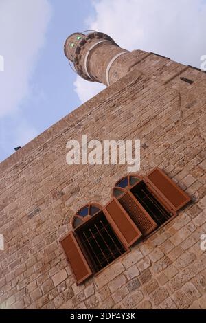 Vista dall'angolo basso del minareto in pietra della storica moschea di al-Bahr e delle finestre ad arco con persiane in legno nella Vecchia Giaffa, adagiate su un cielo luminoso e limpido. Foto Stock
