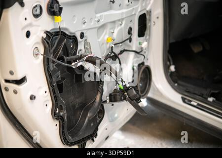 Primo piano di una portiera bianca di un'auto con pannello interno rimosso che mostra il cablaggio e i componenti esposti in un ambiente di carrozzeria. Foto Stock