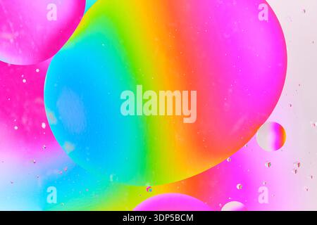 Foto macro astratta di grandi bolle d'olio colorate che galleggiano sulla superficie dell'acqua con un brillante sfondo a gradiente arcobaleno blu, verde e rosa Foto Stock