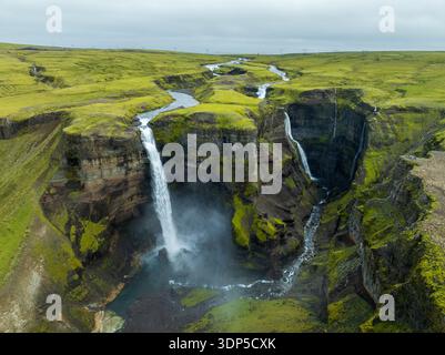 Vista aerea delle cascate della cascata Haifoss tuffati nella gola sottostante, circondato da scogliere verdi e muschiate sotto un cielo nuvoloso, Haifoss, IC Foto Stock