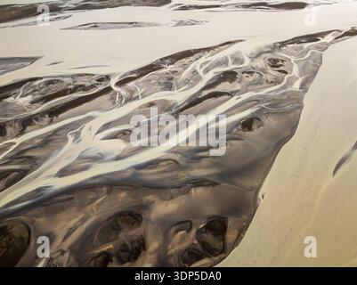 Vista aerea dei fiumi glaciali che intagliano intricati motivi attraverso il paesaggio aspro e contrastante, una danza di luce e ombra sul terrai islandese Foto Stock