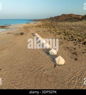 Vista aerea di una linea di tende bianche in netto contrasto con la vasta distesa di spiaggia sabbiosa che incontra il mare turchese, Erisel e Socotra. Foto Stock