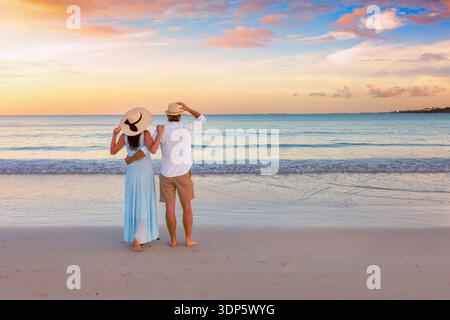 Una coppia romantica e abbracciante in vacanza sorge su una spiaggia tropicale paradisiaca durante lo splendido tramonto Foto Stock
