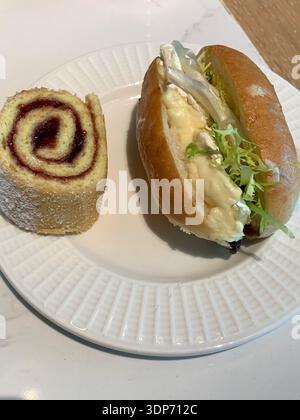 Piatto con una fetta di involtino svizzero ripiena di marmellata dolce e un sandwich con uovo salato e brie con lattuga e lattuga insieme come spuntino misto Foto Stock