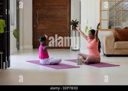 Madre e figlia afroamericana che si stendono su tappetini viola per yoga con bottiglie d'acqua all'ingresso Foto Stock
