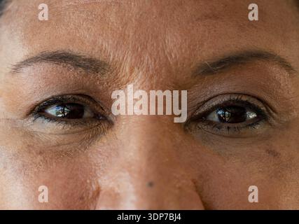 Il viso stretto e ravvicinato mostra pelle ruvida, eyeliner, mascara, mole, riflessi della finestra in studio Foto Stock