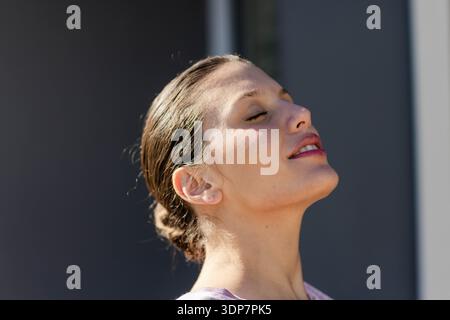 Donna adulta in piedi con gli occhi chiusi, inclinando la testa all'indietro vicino ai pannelli verticali nella parte superiore della lavanda Foto Stock