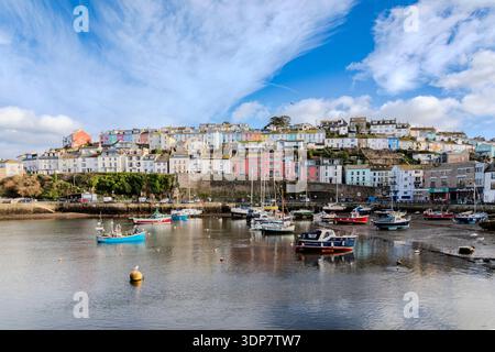 Colina colorata di Brixham, con barche ormeggiate con la bassa marea, sotto un cielo azzurro con nuvole sottili. Foto Stock