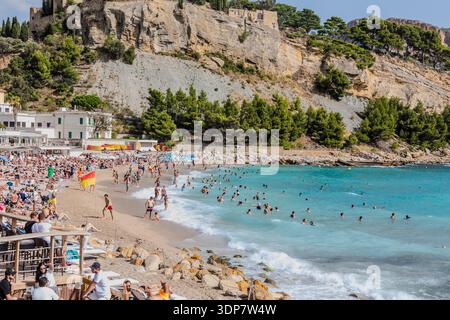 Affollata spiaggia mediterranea a Cassis Provence, con nuotatori in acque turchesi sotto un suggestivo castello sulla cima della scogliera. Foto Stock