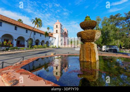 La storica vecchia missione di Santa Barbara, con la sua iconica facciata rosa e i due campanili, si riflette nelle tranquille acque di una fontana di pietra sotto una Foto Stock