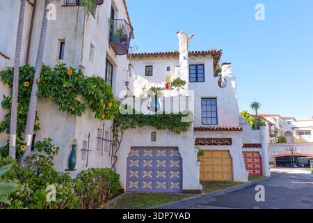 Pittoresco vicolo residenziale di Santa Barbara caratterizzato da edifici in stucco bianco, porte di garage colorate e lussureggianti vigneti verdi con flo giallo Foto Stock
