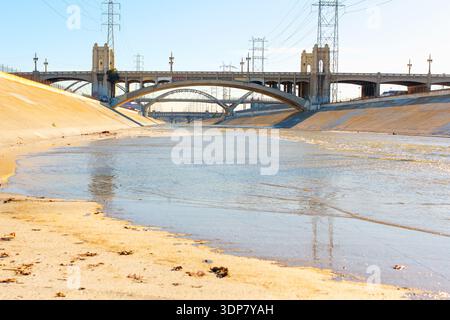 Il fiume Los Angeles scorre attraverso il canale di cemento sotto lo storico viadotto di Sixth Street e gli iconici ponti ad arco sotto i cieli blu della California Foto Stock