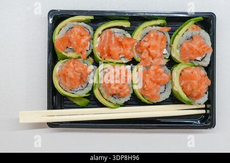 Panini di sushi con salmone e cetriolo in scatola di plastica su sfondo bianco Foto Stock