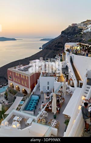 I turisti e la gente del posto mangiano in vivaci ristoranti e bar sulla scogliera a Santorini, in Grecia, godendosi lo splendido tramonto della caldera. Foto Stock