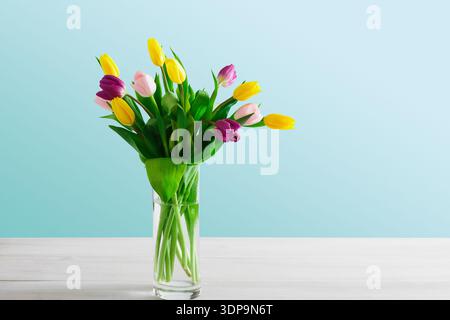 Tulipani colorati in vaso di vetro su un tavolo di legno su sfondo blu Foto Stock