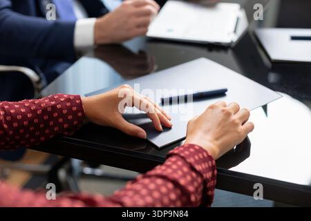 Le mani delle persone sono posizionate su un tavolo coperto di documenti e di una penna. Una persona ha un blocco note pronto, mentre altre si impegnano in una conversazione. Questo è un Foto Stock