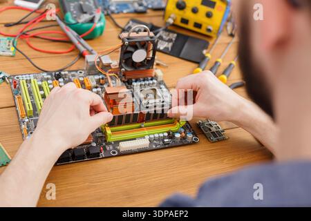 La persona lavora sulla scheda madre del computer in officina durante la sessione di riparazione elettronica Foto Stock