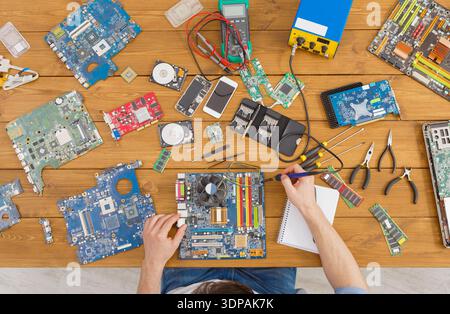 Lavorare con le mani sulle parti del computer e sui circuiti stampati su un tavolo di legno con strumenti e note Foto Stock