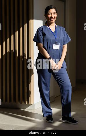 Infermiera che si appoggia a una lastra nella hall e indossa scrub blu cordoncino ID-smartwatch con ombre solari Foto Stock