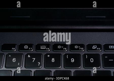 Una persona utilizza un computer portatile in una stanza poco illuminata. L'attenzione è concentrata sui tasti funzione che consentono di eseguire varie attività. Foto Stock
