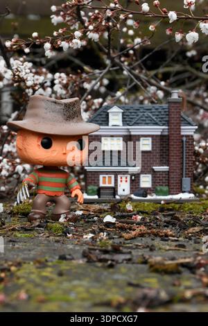 Funko Pop action figure di Freddy Krueger del film horror Nightmare on Elm Street contro la casa di McCallister. Fiori sui rami degli alberi, muschio. Foto Stock