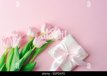 Bouquet di tulipani rosa e confezione regalo con nastro su sfondo pastello. Concetto di regalo per le vacanze primaverili. Vista dall'alto, disposizione piatta. Foto Stock