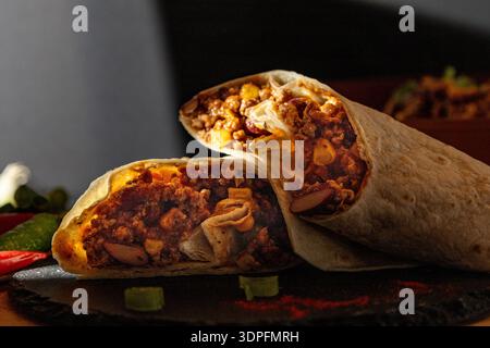 Primo piano di un burrito di manzo appena preparato tagliato a metà, ripieno di carne macinata stagionata, fagioli renali, mais e spezie. Servito su un rustico bo ardesia Foto Stock