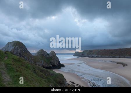 Nuvole di tempesta sopra Three Cliffs Bay con fiume mareale e spiaggia sabbiosa incorniciata da scogliere calcaree sulla penisola di Gower, Swansea, Galles, Regno Unito. Foto Stock