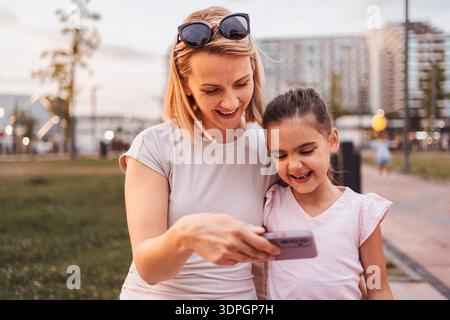 Madre e figlia guardano lo smartphone e sorridono nel parco Foto Stock