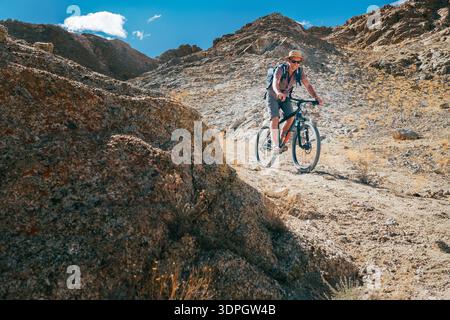 Ciclismo su mountain bike lungo lo stretto percorso cliffy in Ladakh, India, caratterizzato da ripidi pendii rocciosi e massicci creste di montagna sotto la b Foto Stock