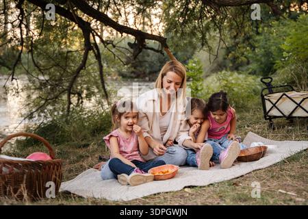 Madre che si diverte a fare un picnic sul fiume con le sue tre figlie Foto Stock