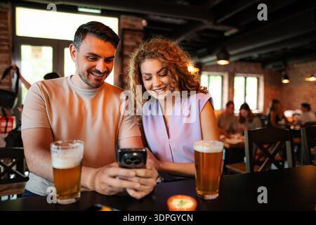 Coppia che si gusta la birra e guarda lo smartphone al pub Foto Stock