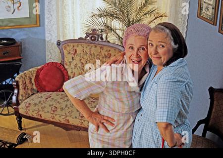 Due amiche anziane si stanno avvicinando e sorridono in un salotto d'epoca. Sono vestite con abiti di colore chiaro e enjo Foto Stock