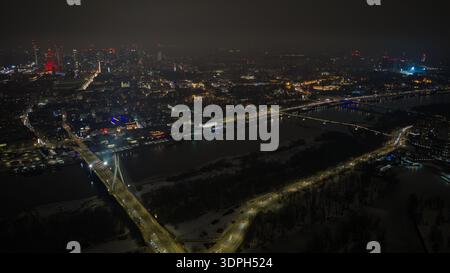 La vista aerea notturna di Varsavia mostra il fiume Vistola, il ponte Swietokrzyski, i ponti illuminati, il Palazzo della Cultura e della Scienza, la città vecchia e le rive innevate con Foto Stock