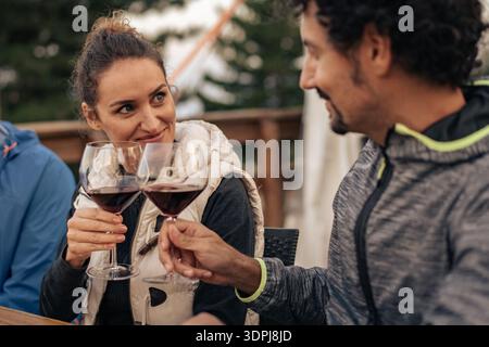 Primo piano di una coppia matura che brinda un bicchiere di vino rosso mentre si guardano l'un l'altro durante una cena all'aperto. Un autentico momento di stile di vita che esprime emotio Foto Stock