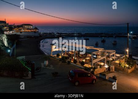 Panormos, Creta, Grecia - 6 settembre 2025: Persone che cenano al ristorante sul mare al tramonto con un cielo colorato sopra il Mar Mediterraneo nel villaggio di Foto Stock