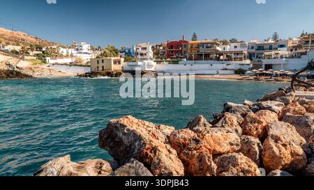 Panormos, Creta, Grecia - 9 settembre 2025: Vista costiera del villaggio di Panormos con porto, case sul mare e ombrelloni lungo il Mediterraneo Foto Stock