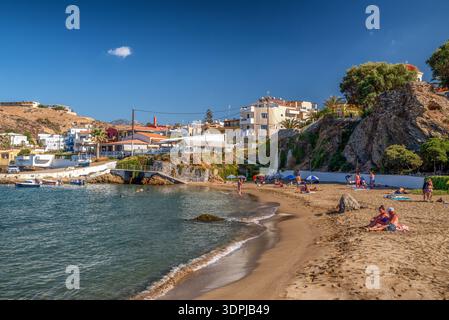 Panormos, Creta, Grecia - 9 settembre 2025: Turisti che si rilassano sulla spiaggia di sabbia nel villaggio di Panormos con case costiere e mare Mediterraneo nel bac Foto Stock