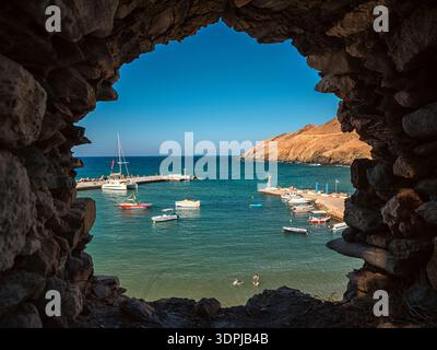 Panormos, Creta, Grecia - 9 settembre 2025: Veduta del piccolo porto con barche e nuotatori incorniciati da una grotta rocciosa naturale che si apre nella villa Panormos Foto Stock