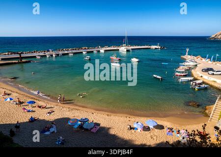 Panormos, Creta, Grecia - 9 settembre 2025: Spiaggia sabbiosa con i turisti che nuotano e si rilassano vicino al porticciolo con barche ancorate a Panormos vil Foto Stock